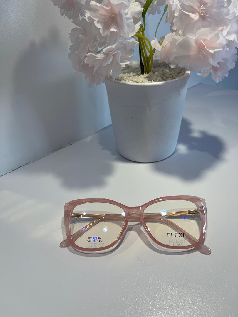 Pink eyeglasses on a white surface with a potted plant in the background