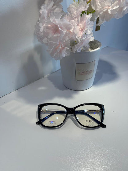 Black-framed glasses on a white surface with a potted plant in the background