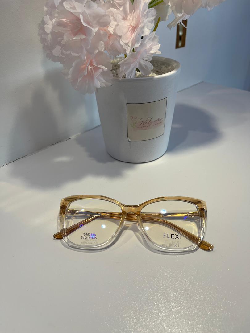 Gold-framed glasses on a white surface with a potted plant in the background